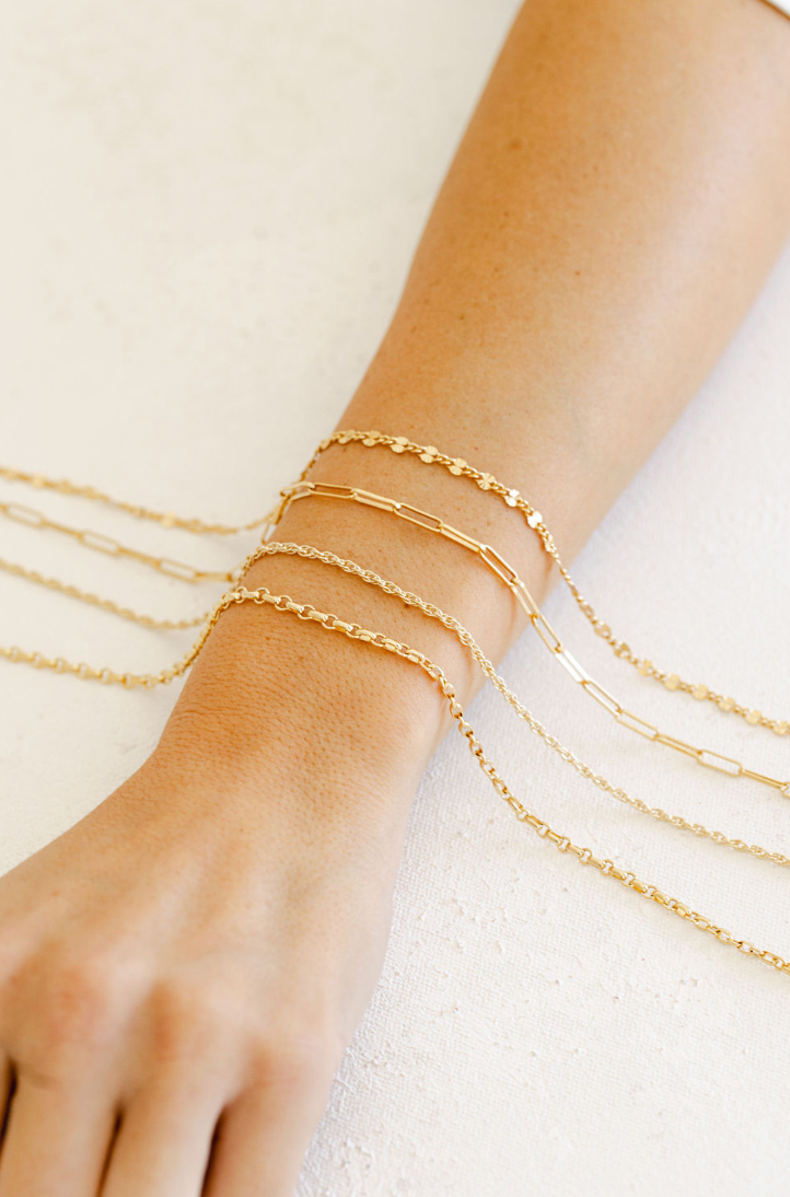 Gold permanent jewelry bracelets on a wrist against a light background