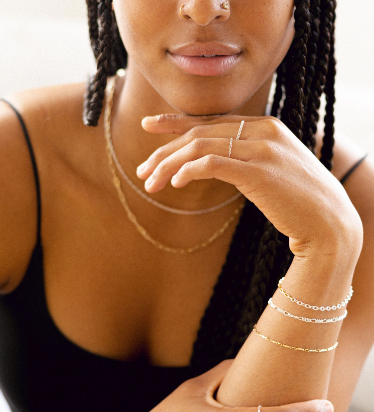 Woman wearing gold jewelry including a necklace, bracelet, and ring.